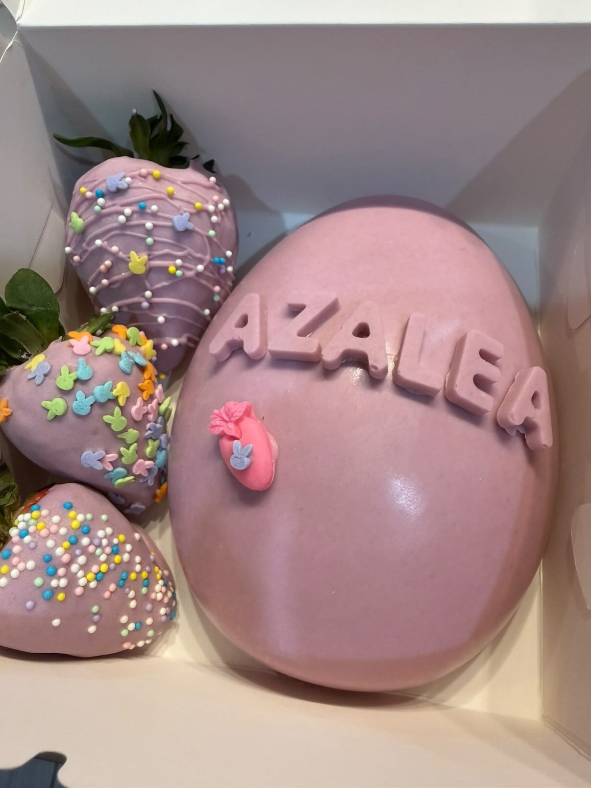 Pastel pink Easter strawberries with bunny sprinkles beside a hand-stamped chocolate egg.