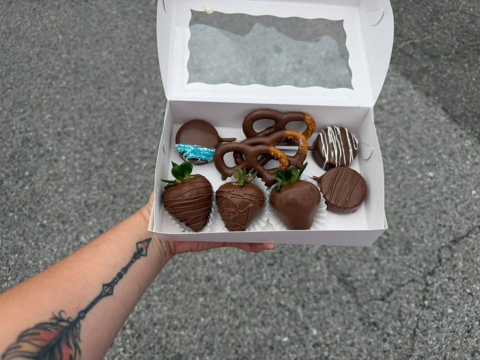 A hand holding a window box of milk-chocolate strawberries, dipped Oreos, and a chocolate pretzel.