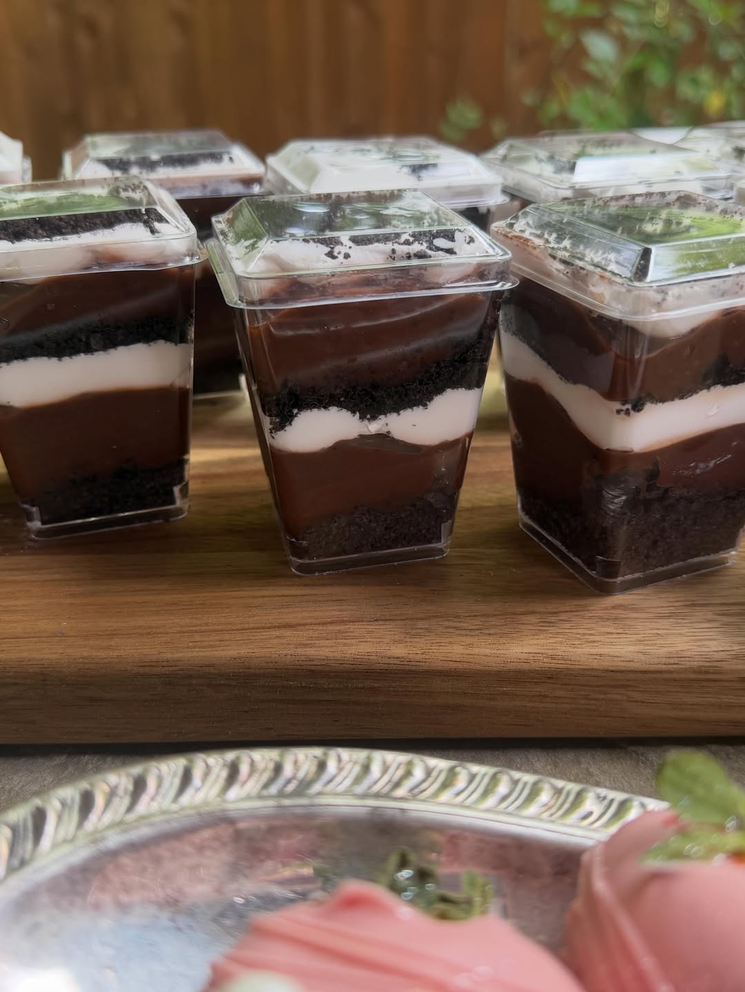 Layered chocolate-and-Oreo dessert cups lined up on a wooden board.