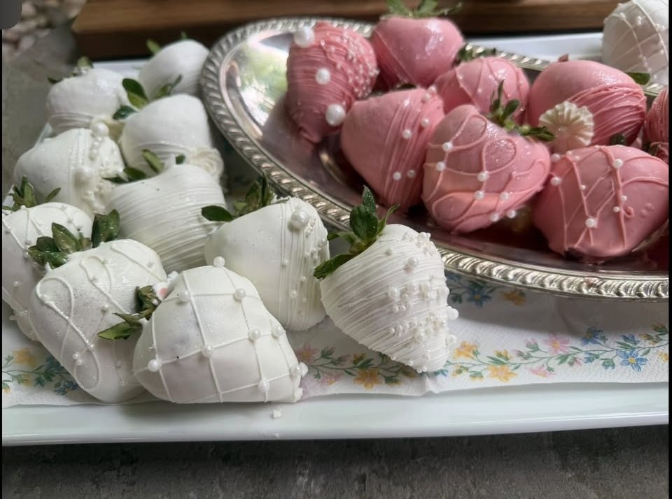 Pink and white chocolate-dipped strawberries finished with sugar pearls on a silver tray.