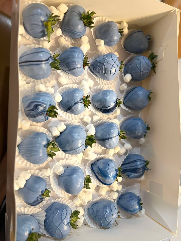 Dusty blue chocolate-covered strawberries with white drizzle, boxed on a bed of mini marshmallows.
