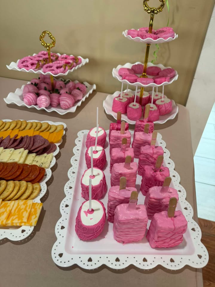 A pink dessert table — tiered cake pops, dipped strawberries and assorted treats on white platters.