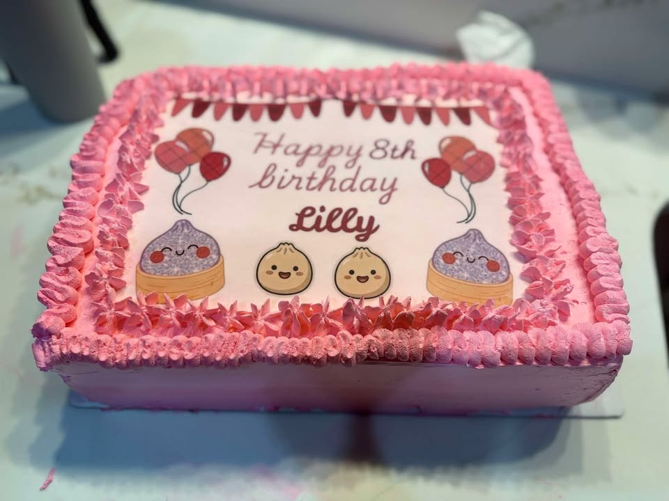A pink buttercream sheet cake with ruffled piping reading “Happy 8th birthday Lilly”.