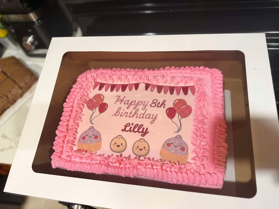 The pink “Happy 8th birthday Lilly” sheet cake boxed in a window bakery box.