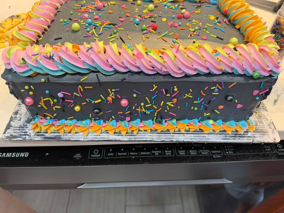 A black sheet cake finished with rainbow buttercream piping and confetti sprinkles.