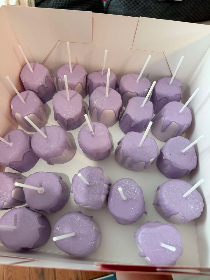 Lavender cake pops lined up in a bakery box.