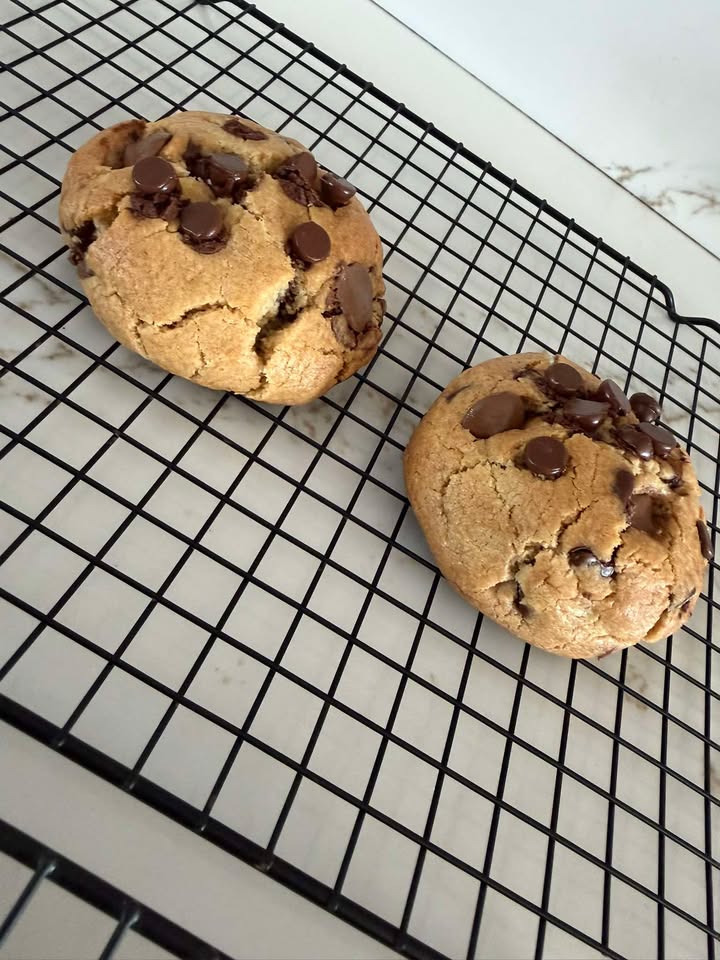 Two freshly baked chocolate chip cookies cooling on a wire rack.